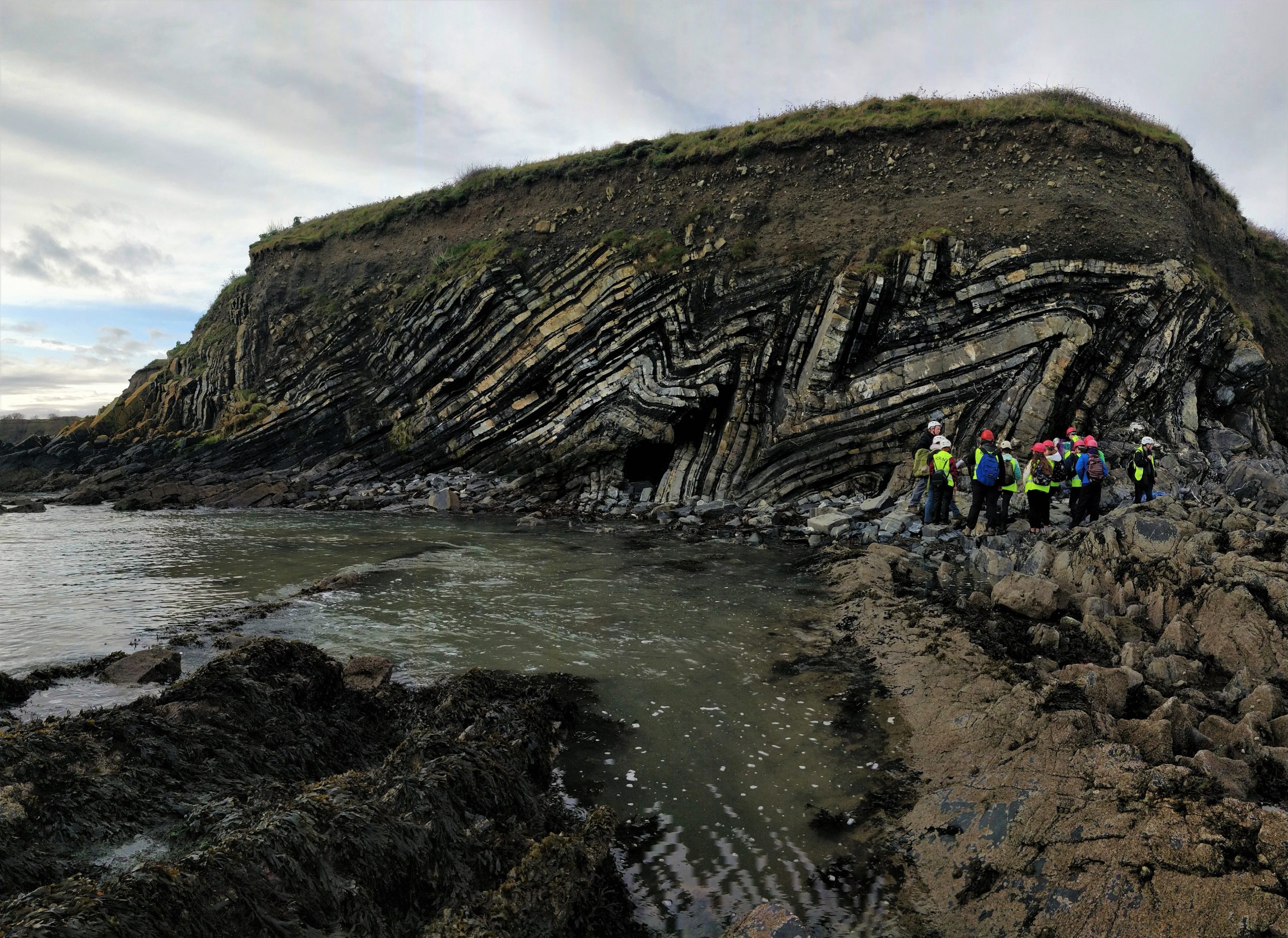 A group of women look at geological folds on a rock in Ireland.