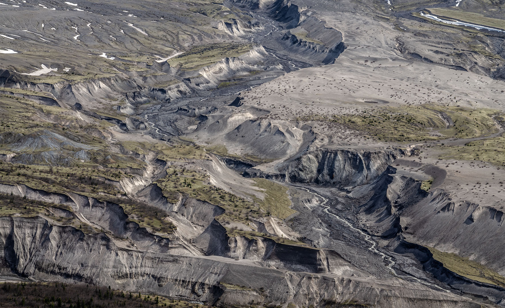 Aerial view of modern canyons carved through dark gray unconsolidated volcanic deposits with sparse vegetation in the area.