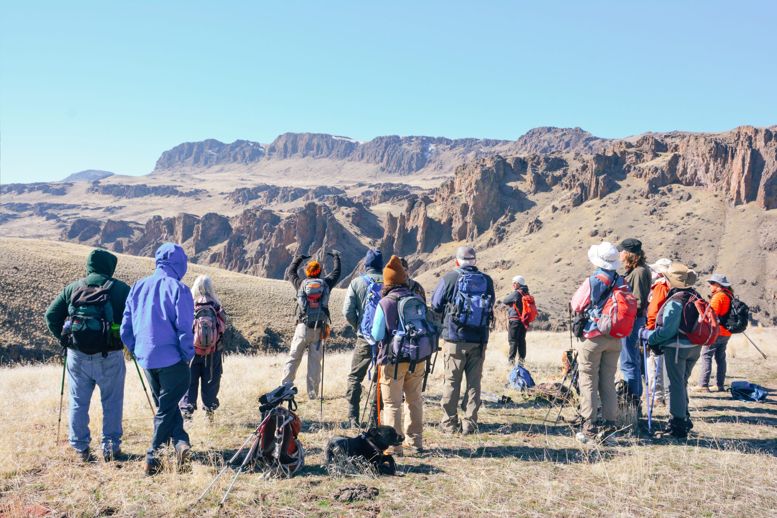 15 people at a field trip looking at large rock outcrops in the distance.