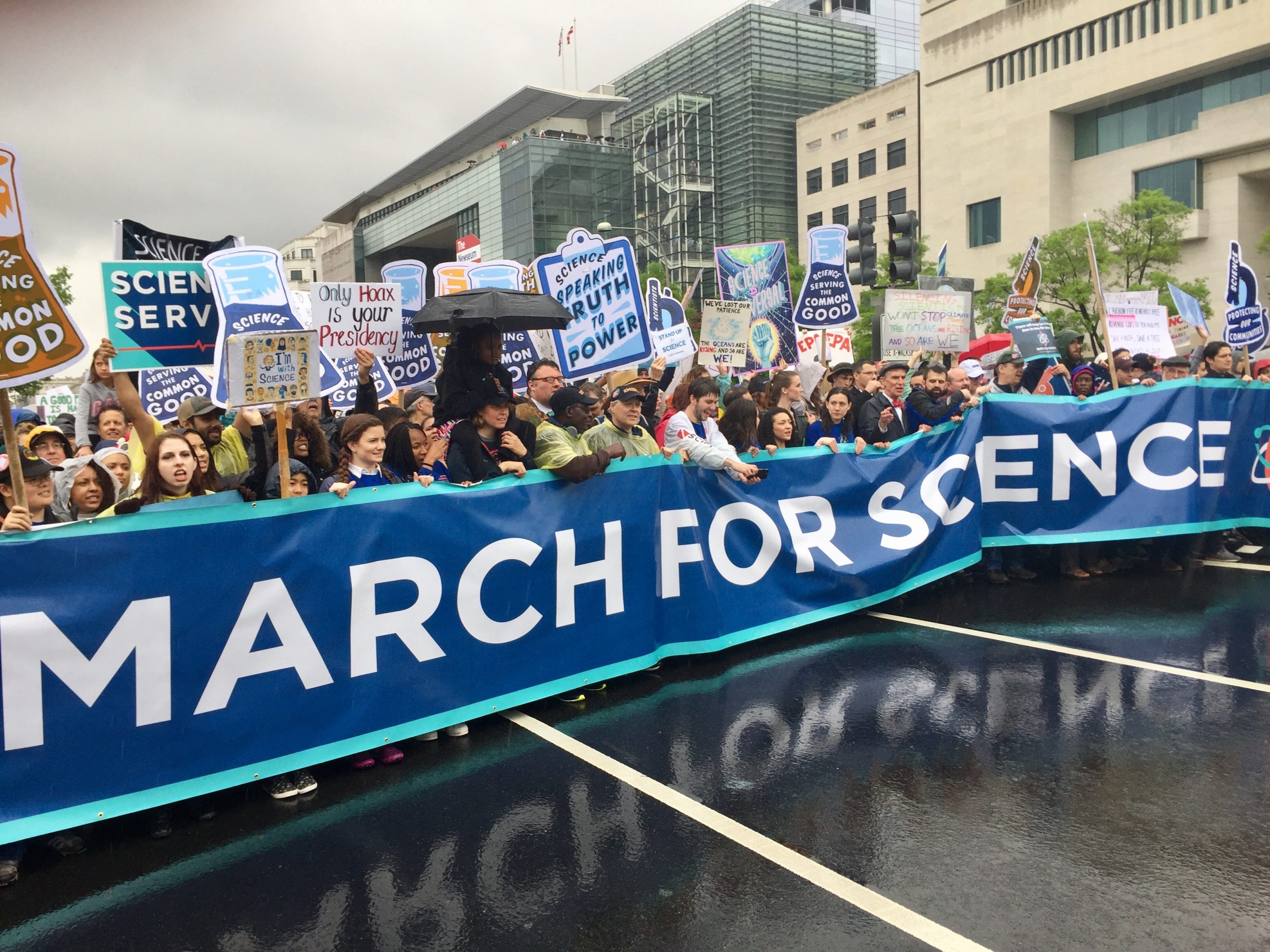 Huge crowd of people marching on the street holding a banner that says "March for Science"