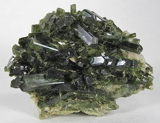 A sample of elongated dark green crystals clustered together in the same sample.