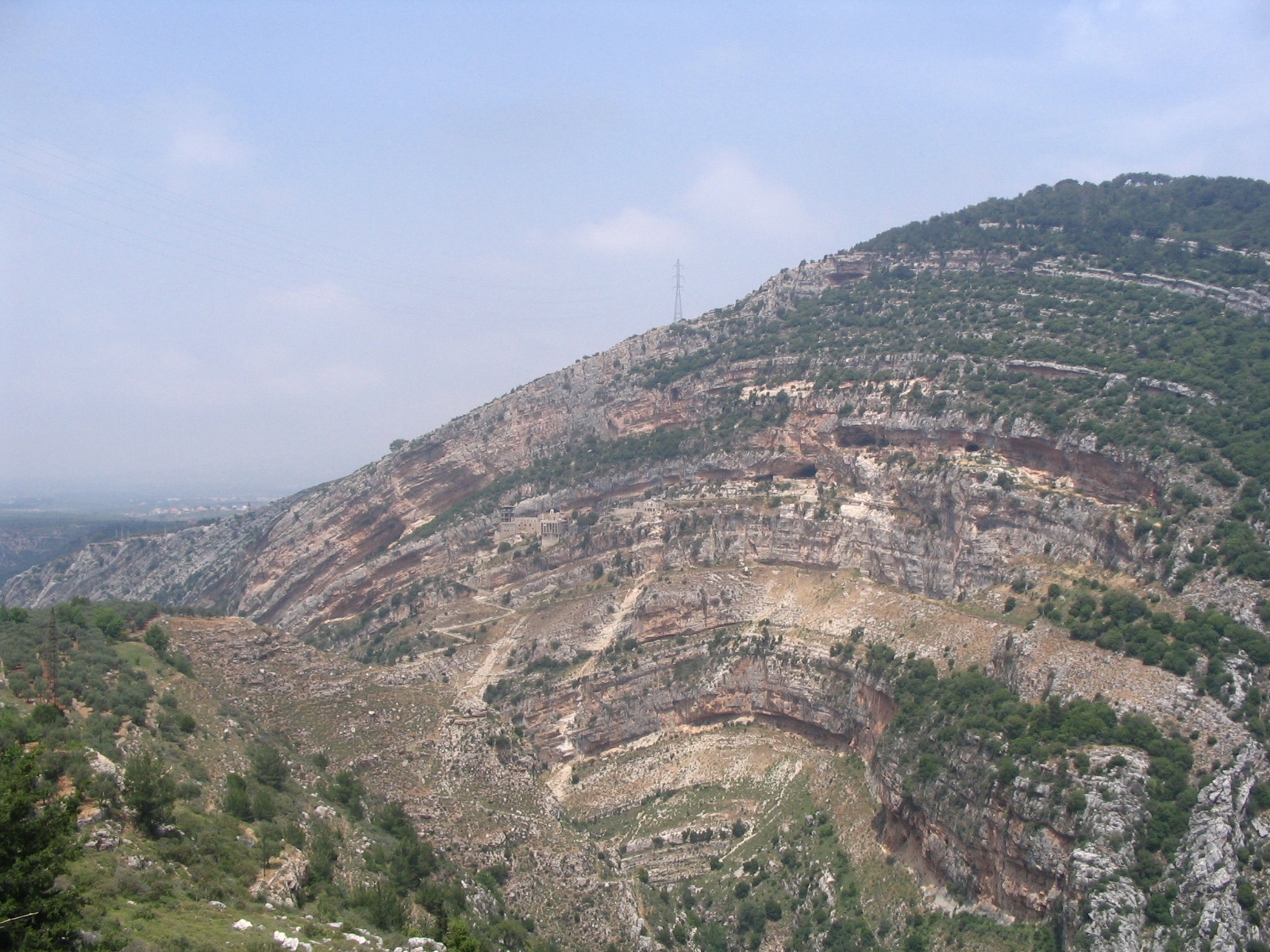 View of a hillside with exposed sedimentary layers that form an arch shape.