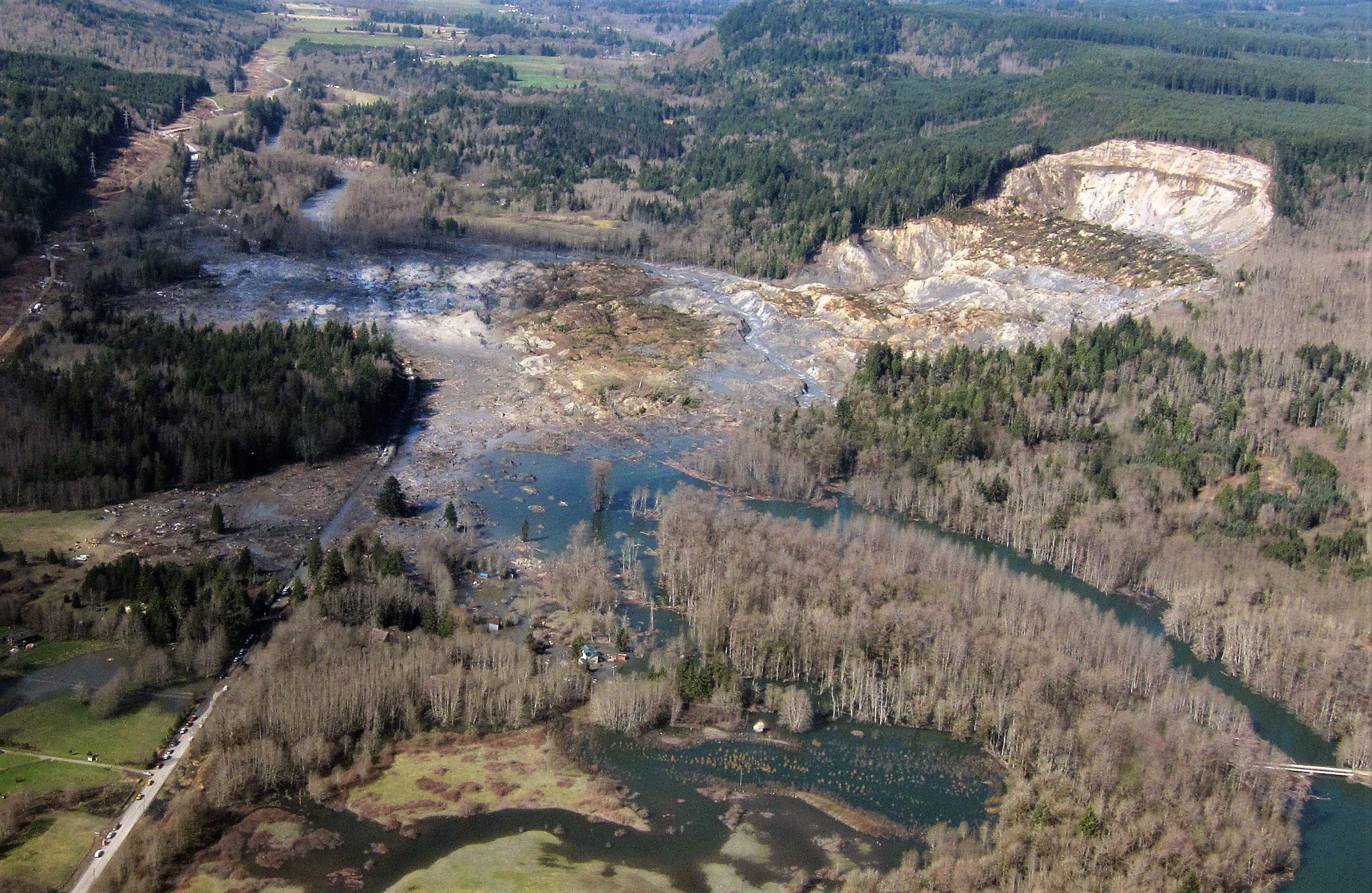 Aerial photo of large slide scarp with debris at the bottom of the hillside covering an entire river and damming it.