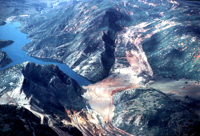 Aerial photo of vegetated mountains with a river running through them; a large tan landslide can be seen covering the river and damming it, creating a lake.