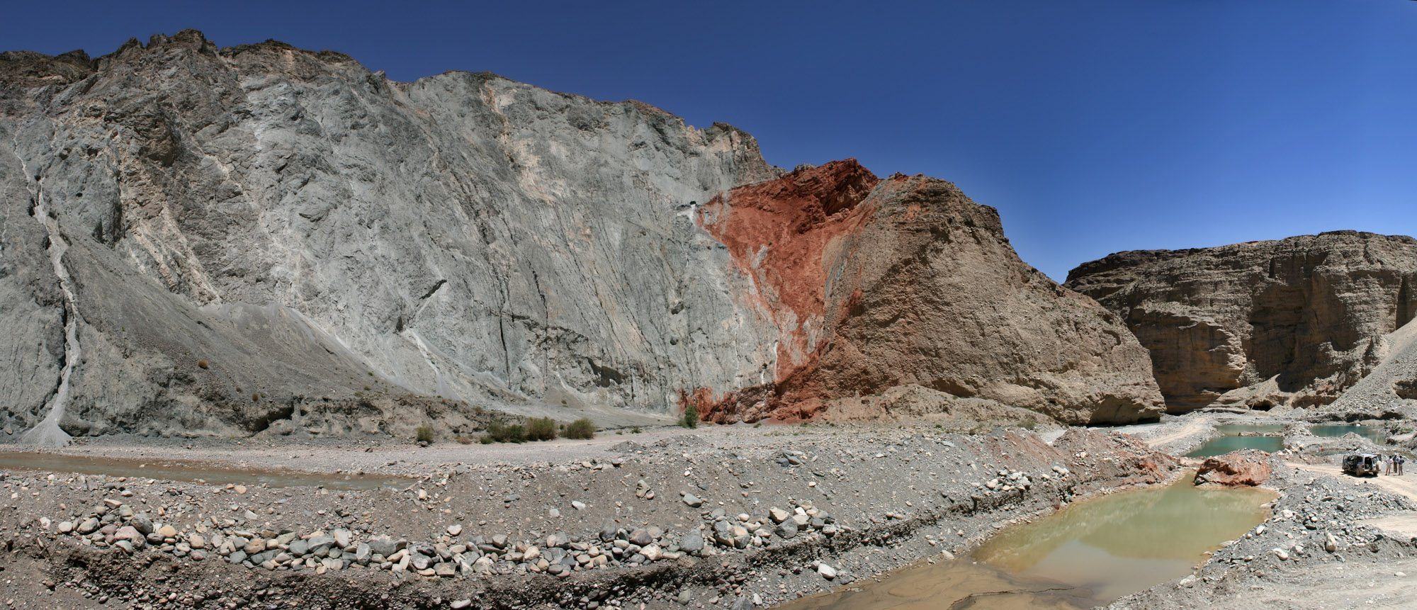 View of a cliffside with gray rocks on the left-hand side; red rocks are to the right of the gray rock with a fault plane visible below the red rocks, angled from the lower left to upper right; below and on the right side of the fault are brown sedimentary rocks.