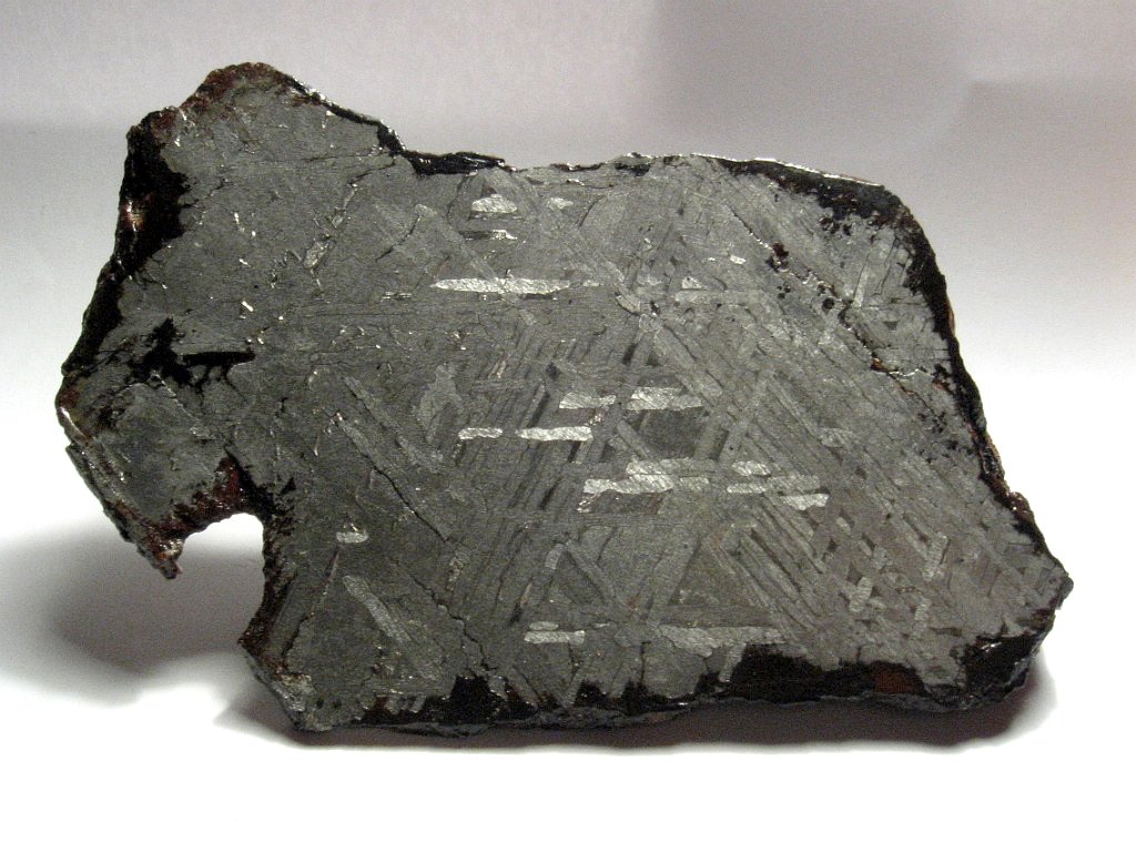 Photograph of a cut and polished face of a silvery gray meteorite. There is a distinct pattern of criss-crossing lines on the polished surface.
