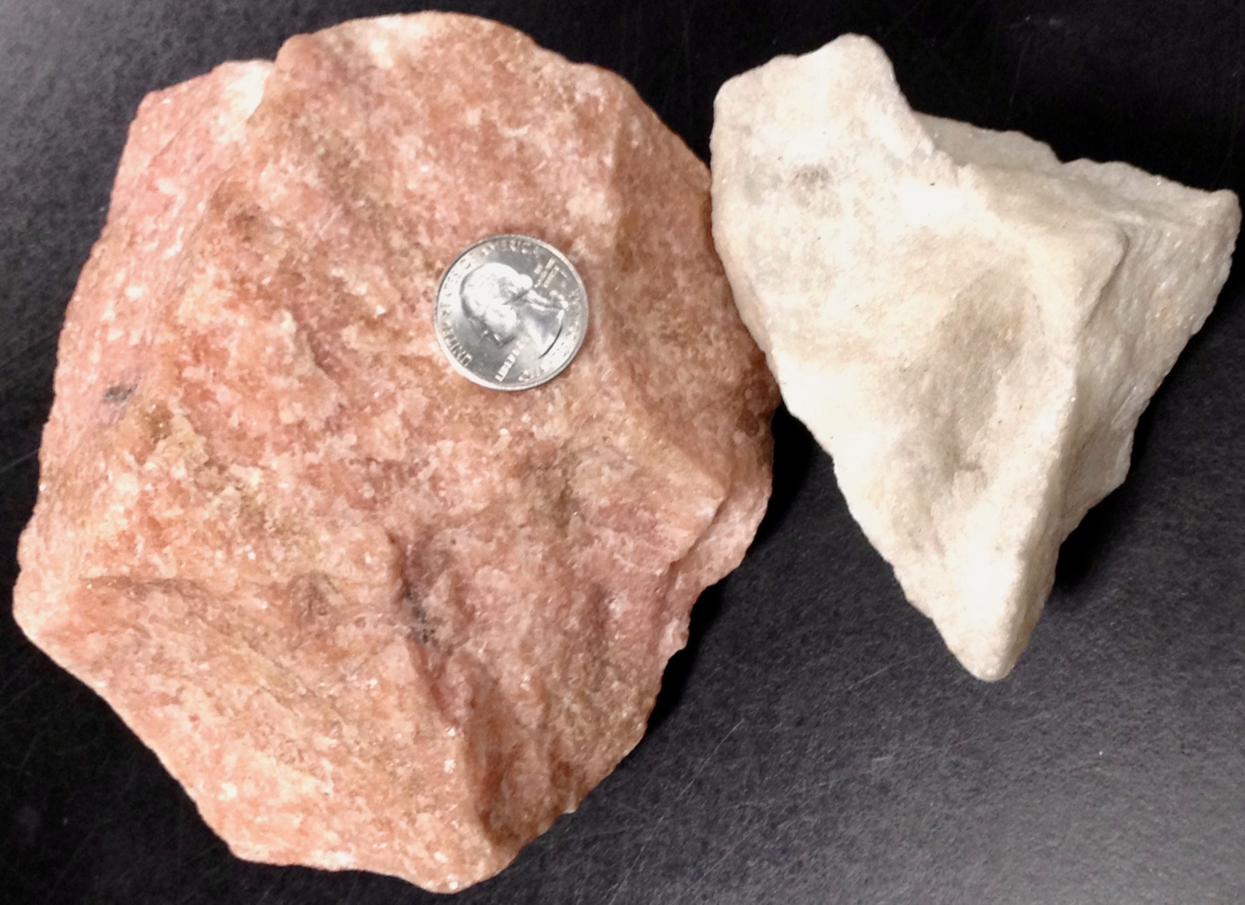 Two chunks of rock, one pink in color and the other white in color; both have interlocking crystals; a US quarter rests on the pink sample for scale.
