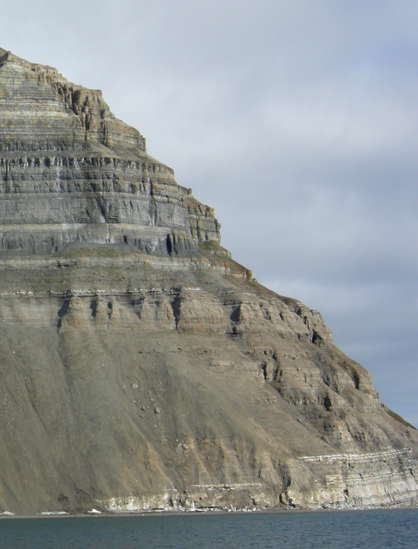 Sloping cliffside with flat-lying layers of tan and brown sedimentary rocks.