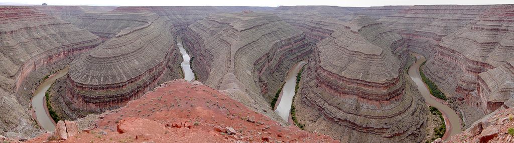 Panoramic view of an S-shaped meandering river that flows at the base of tall canyons.