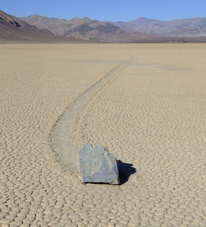 A large gray rock has slid over the light tan playa surface leaving a track in the playa.