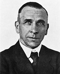 Black and white headshot of a man in a suit and tie.