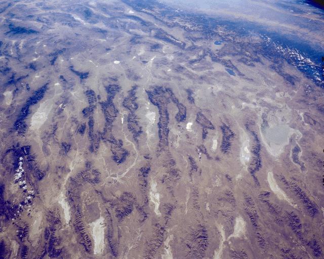 Satellite photo of a tan landscape that has long ridges and valleys.