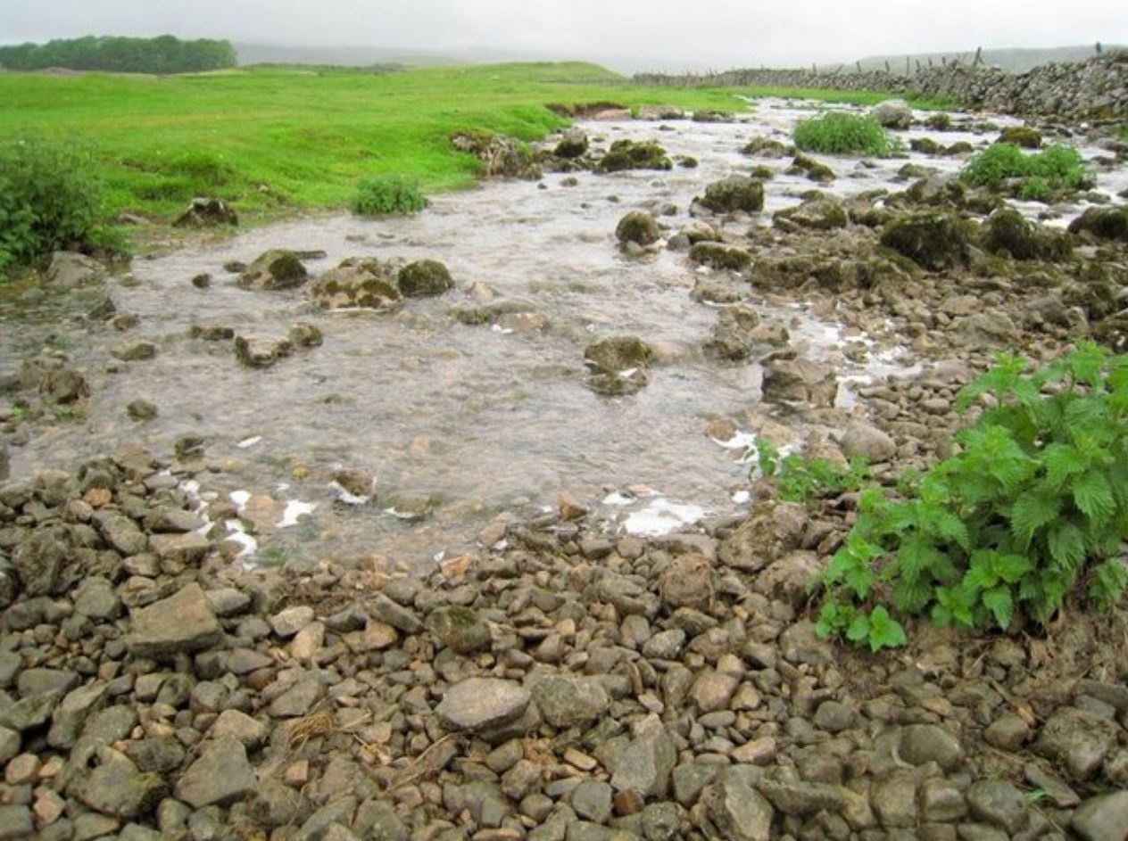 A stream disappears into gravel at the foreground of the photo.