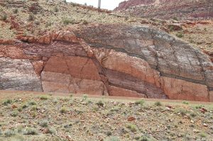 Roadcut cliffside outcrop of multicolor sedimentary beds offset by a normal fault; on either side of the fault, the rocks on the right-side hanging wall have moved downward relative to the rocks on the left-side foot wall.