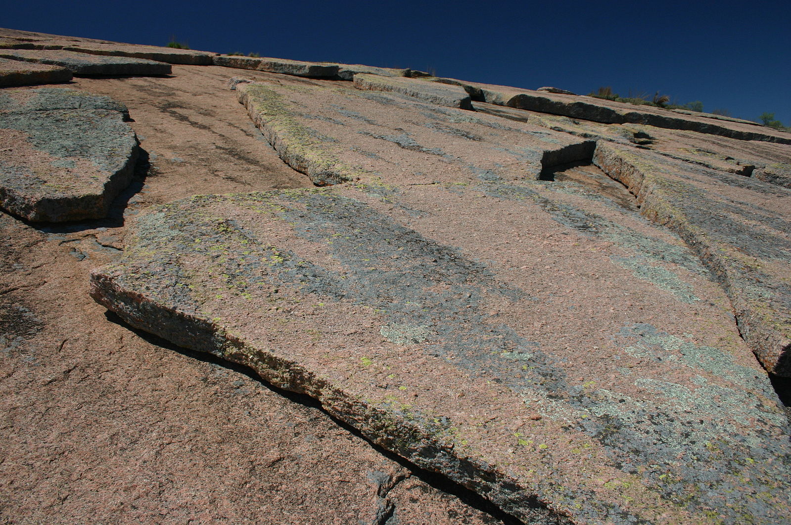 A layer of broken slabs of rock lying on top of a larger landscape of domed rock. The rocks are reddish-tan and gray.