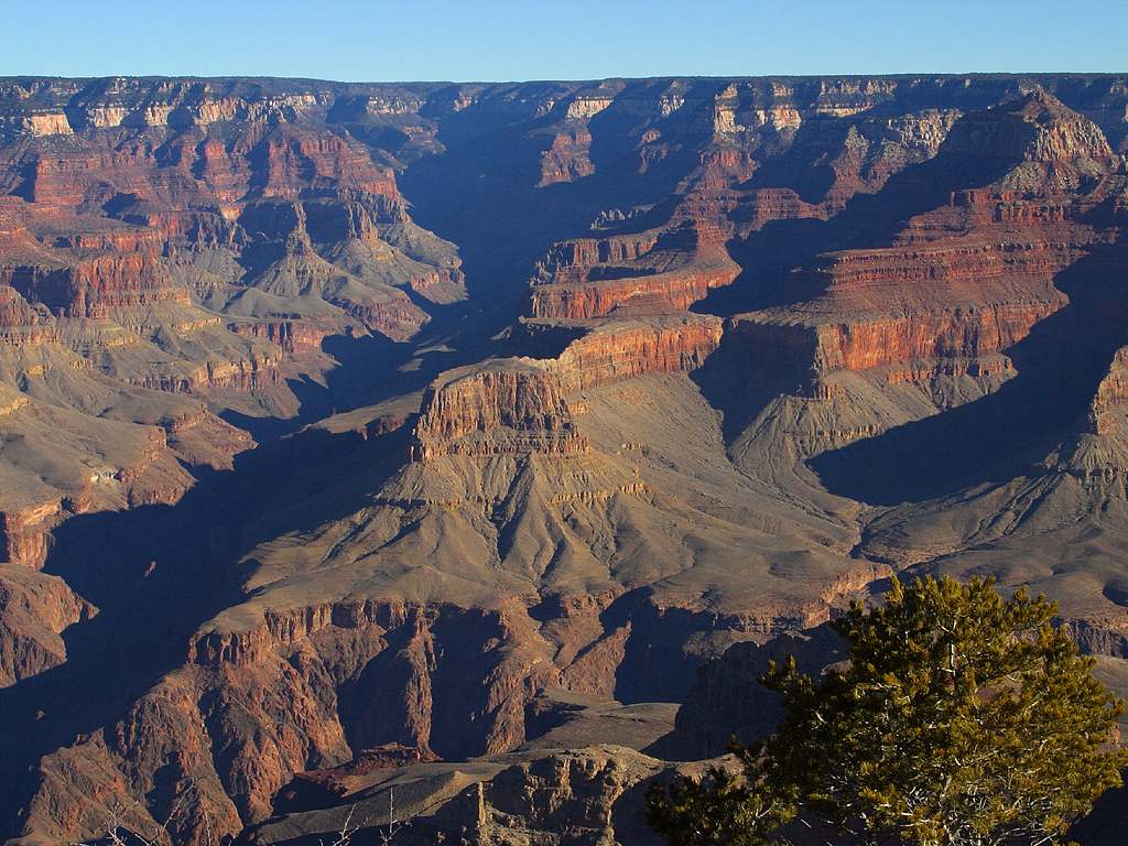 Canyon with many cliffs and slopes throughout; there is a visible band of whitish rock near the top of the canyon walls and the slopes are dark gray to black. The rest of the cliffs range in color from red to tan to brown.