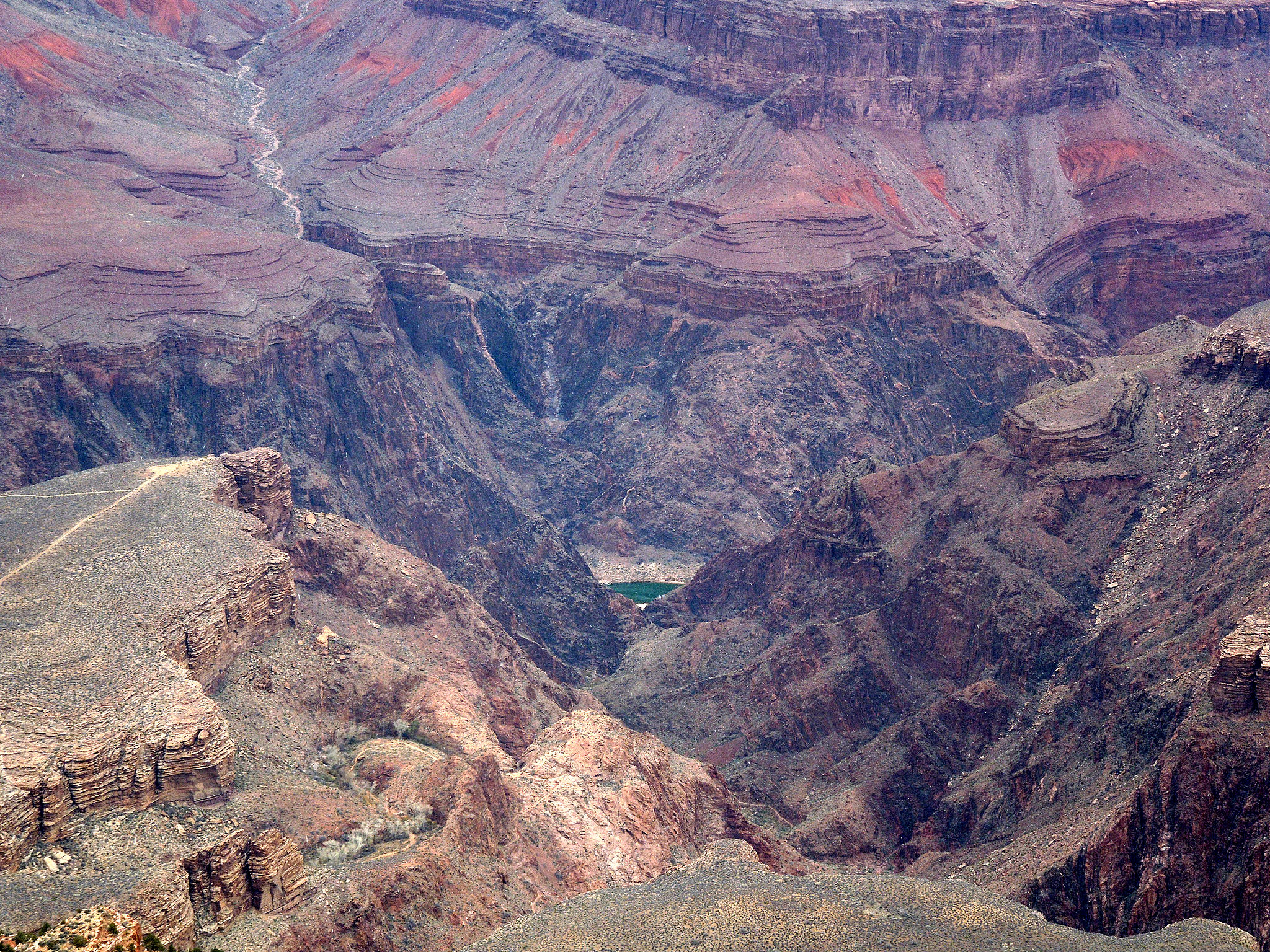 View of canyon walls of the Grand Canyon in which you can see flat-lying layers of reddish sedimentary rock overlying dark brownish rocks that don't have any layering.