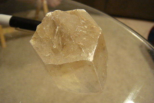 Cream-colored translucent crystal with 6 sides. A marker sits next to the sample for scale.