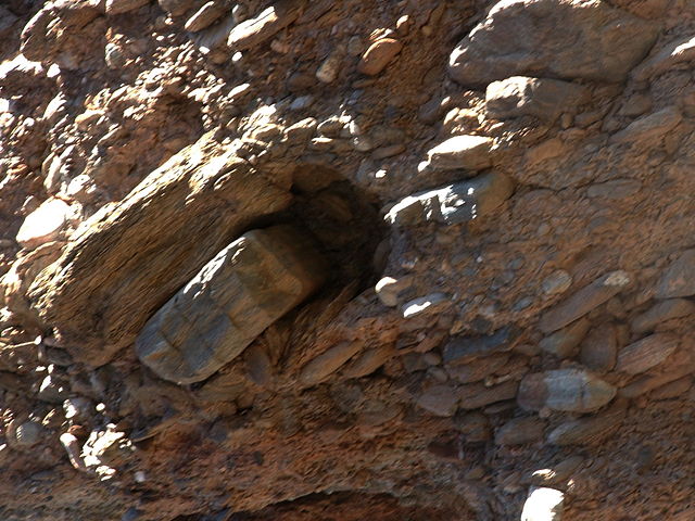 Tan to brown conglomerate with rounded cobbles embedded parallel and stacked on each other.