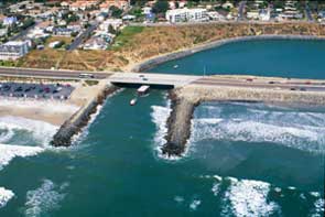 Two parallel jetties extending into the ocean; on the left side of the left jetty is a buildup of sand while the other sides of the jetties do not have the same buildup.