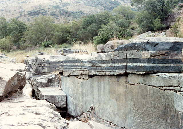 Vertical outcrop of alternating tan and black horizontal layers.