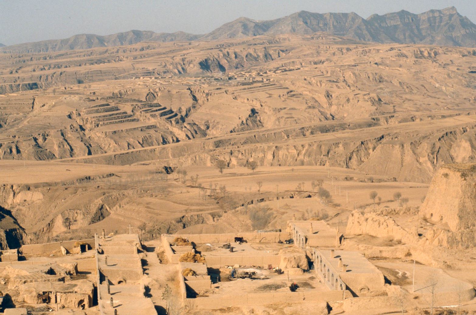 Tan landscape of plateaus and canyons with buildings carved into the stone.