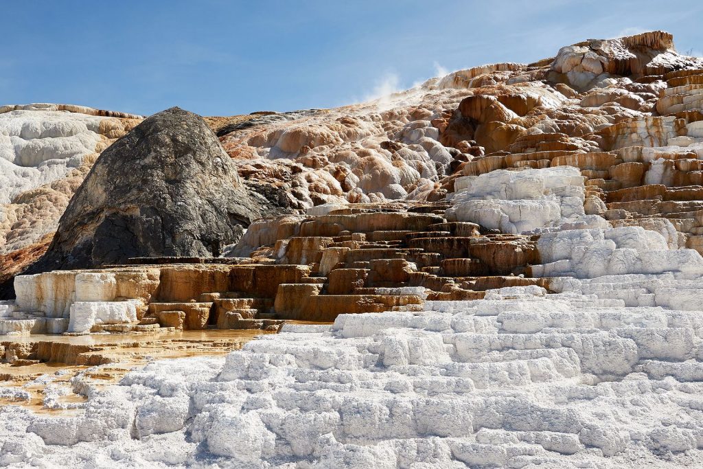 White and brown natural steps with steam rising near the back; the brown steps have a coating of liquid and organic material while the white steps are dry and chalky in appearance.