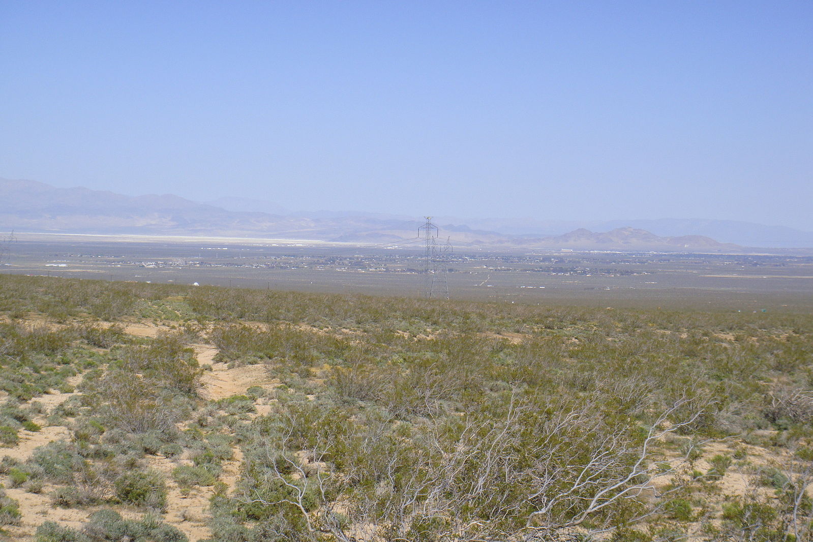 Desert landscape covered in low scrubby vegetation. A town can be seen in the distance.