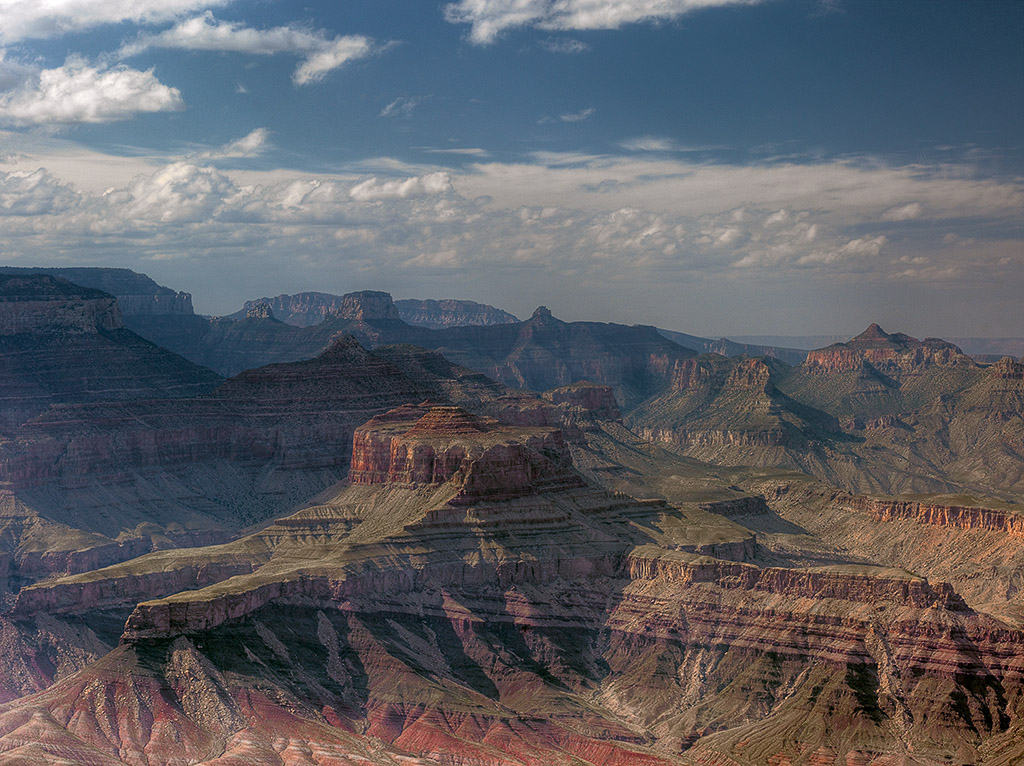 View of canyon walls of the Grand Canyon in which you can see reddish and gray flat-lying sedimentary rock layers overlying shallowly dipping tan and gray sedimentary rock layers.