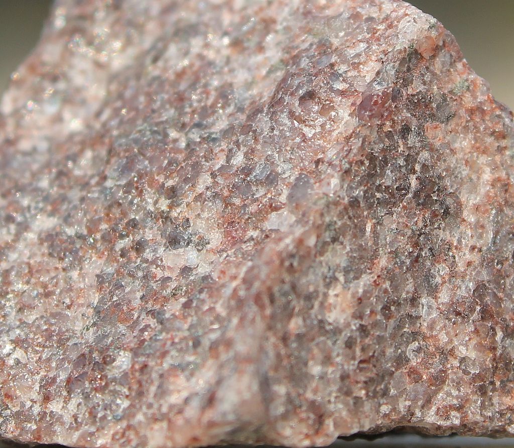 Zoomed-in view of a chunk of pinkish tan rock with interlocking glassy crystals.