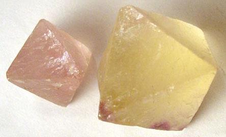Two crystals side by side. Left: pink, transluscent, smaller, shape mimics 2 pyramids glued together at their bottoms. Right: same as left but bigger and yellow