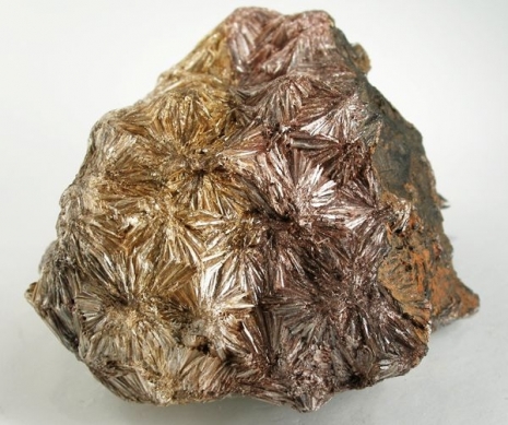 Many bronze colored, reflective, short crystals that have a center and fan out. All start and stop randomly to form a rock shape