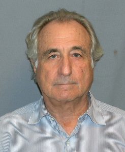 A photograph of Bernie Madoff standing in front of a blue background.