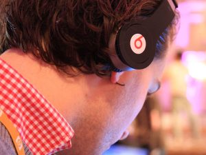 A close profile photograph of a person wearing a pair of black Beats headphones. The person is looking down, with the headphones in the center of the photograph.